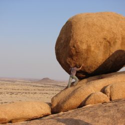 man pushes boulder up a hill