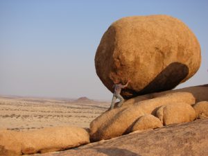 man pushes boulder up a hill