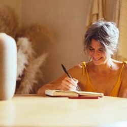 a woman journalling, smiling, at a desk at home